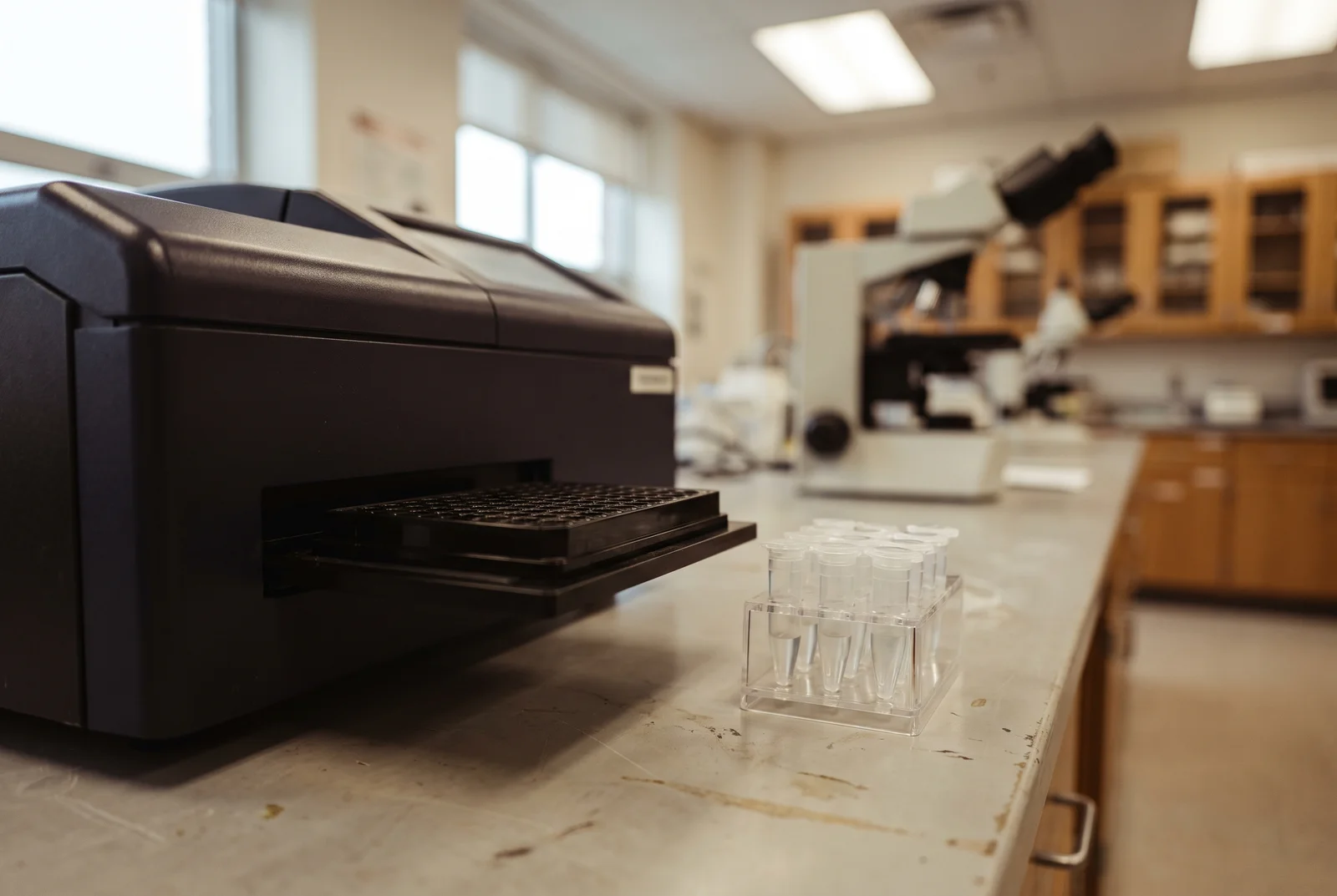 AI-generated illustration of a black microplate reader with an extended tray beside clear sample tubes on a laboratory bench